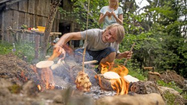 Ein Vater sitzt vor dem lodernden Lagerfeuer, im Hintergrund steht ein begeistertes Kind... &copy; Waldwelt Skywalk Allg&auml;u