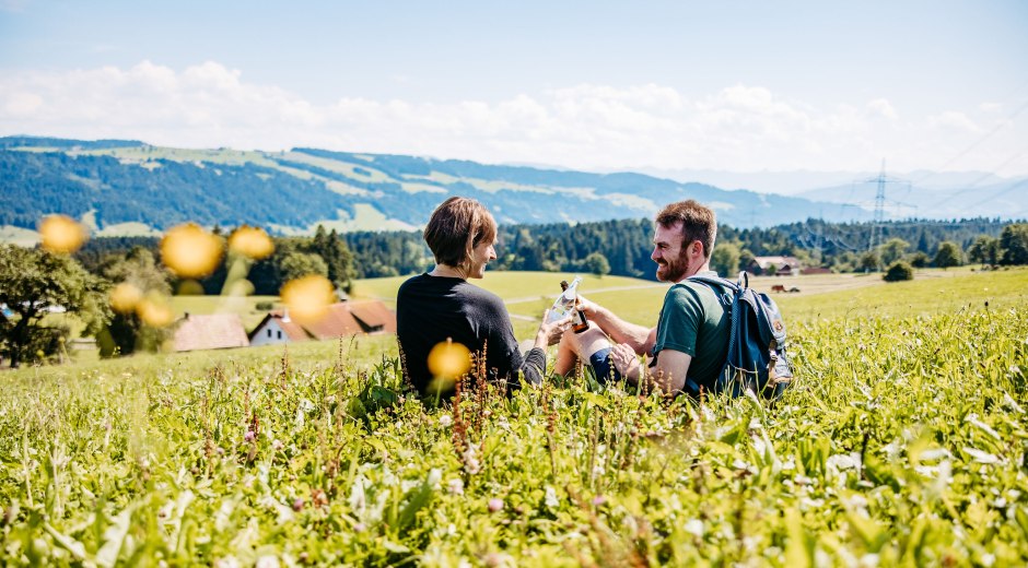 Zwei Personen sitzen auf einer Wiese und trinken Wasser und Bier aus der Region Westallgäu und genießen dabei die Aussicht. © Frederick Sams Zwei Personen sitzen auf einer Wiese und trinken Wasser und Bier aus der Region Westallgäu und genießen dabei die Aussicht. © Frederick Sams