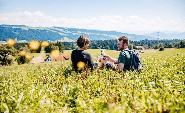 Zwei Personen sitzen auf einer Wiese und trinken Wasser und Bier aus der Region Westallg&auml;u und genie&szlig;en dabei die Aussicht.  &copy; Frederick Sams