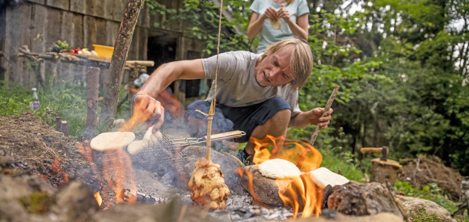 Ein Vater sitzt vor dem lodernden Lagerfeuer, im Hintergrund steht ein begeistertes Kind... &copy; Waldwelt Skywalk Allg&auml;u