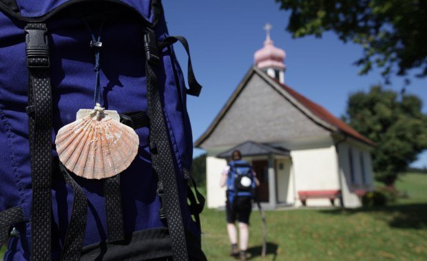 Kraftquelle Allgäu: Pilgern im Westallgäu, Bild mit Wanderer, Rucksack mit Jakobsmuschel und Kapelle.